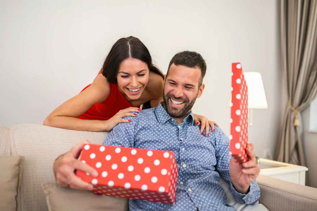 What to get men for Valentines Day - Man opening red gift box with woman standing behind smiling