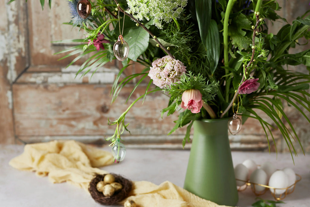 Easter and flowers arrangement in green vase on table next to gold easter eggs