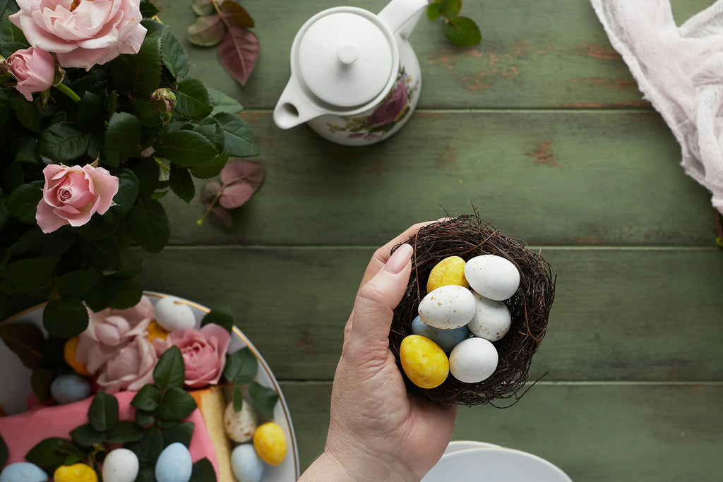 Hand holding basket of coloured easter eggs next to pink flower bouquet