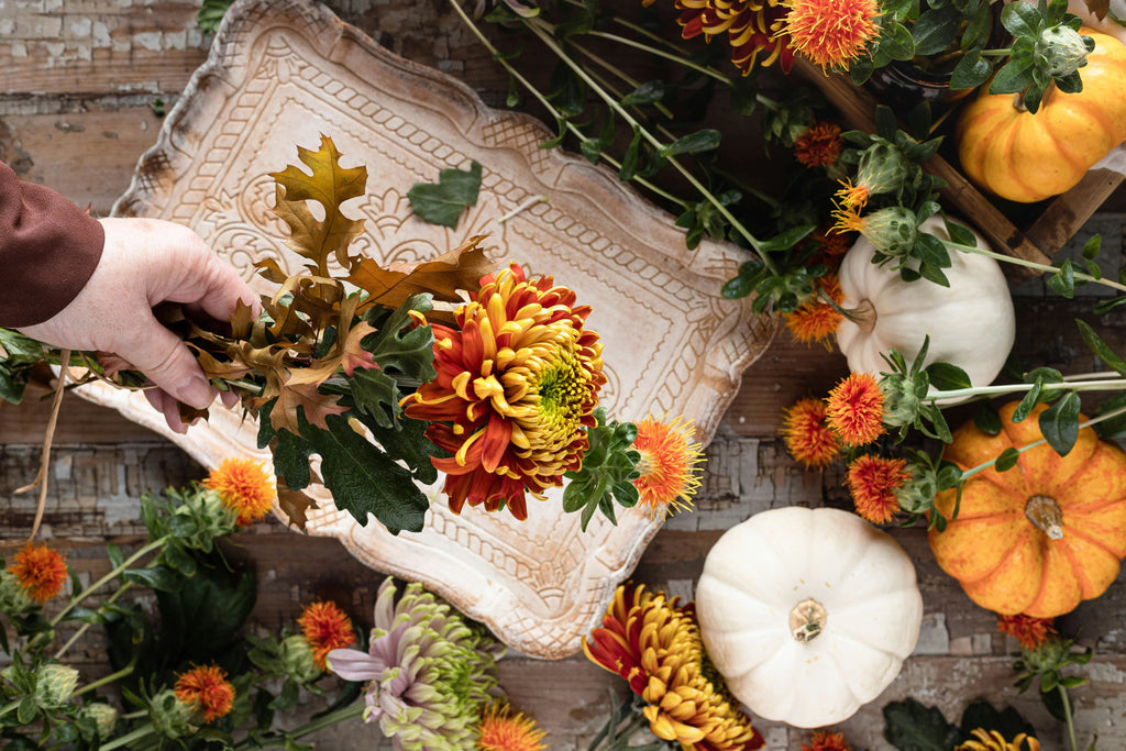 Photo of a hand holding a bouquet of flowers above a table covered with wild flowers and pumpkins
