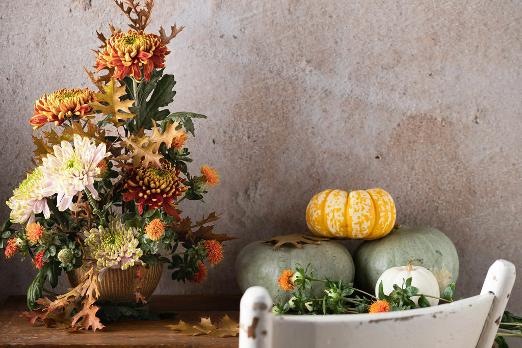 Photo of a Thanksgiving centerpiece next to pumpkins and leaves on a wood table