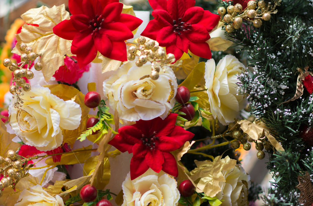 Photo of red poinsettias and white roses with gold accents in a bouquet next to green pine
