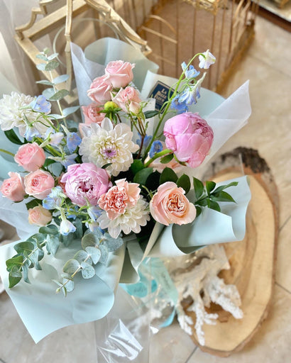 Photo of a mixed bouquet of peach, pink, and white flowers, wrapped in paper by La Belle Fleur