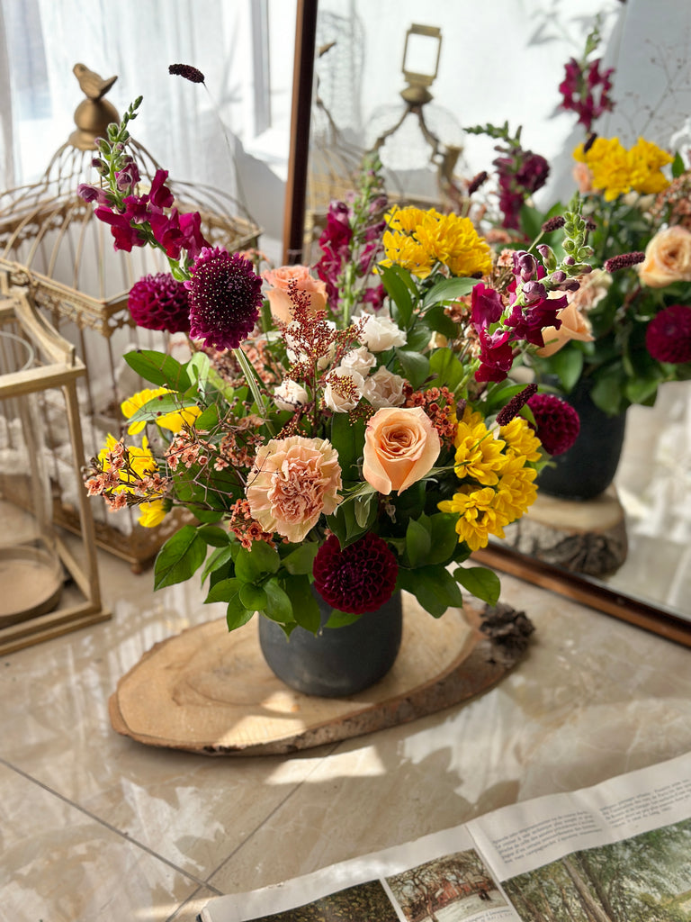 Fall Garden Wild Flower Arrangement by La Belle Fleur with peach roses, yellow flowers, purple flowers, and greenery in a grey vase
