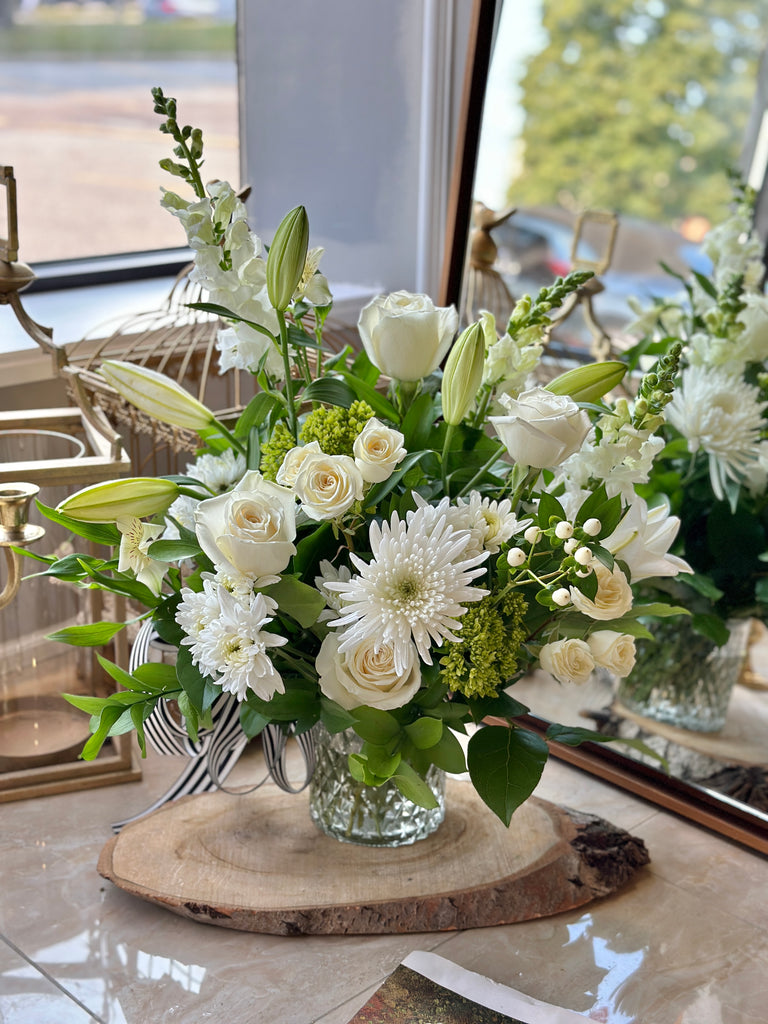 Photo of a large white flower arrangement in a glass vase on a wood slab