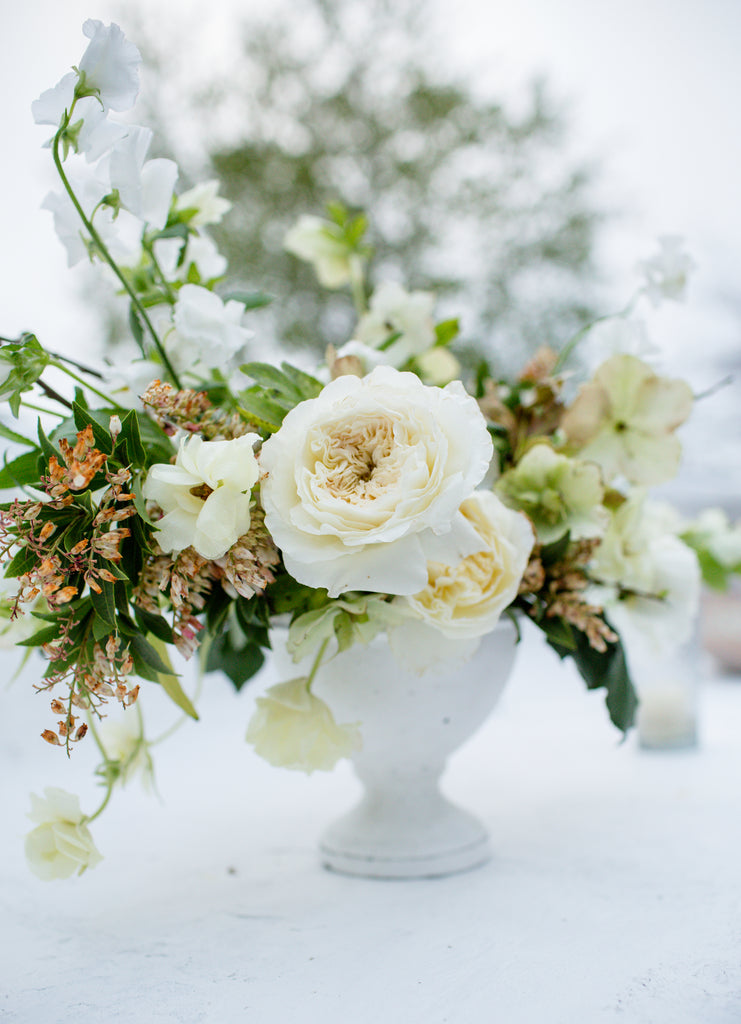Photo of a white rose arrangement in a white ceramic vase on a wedding table