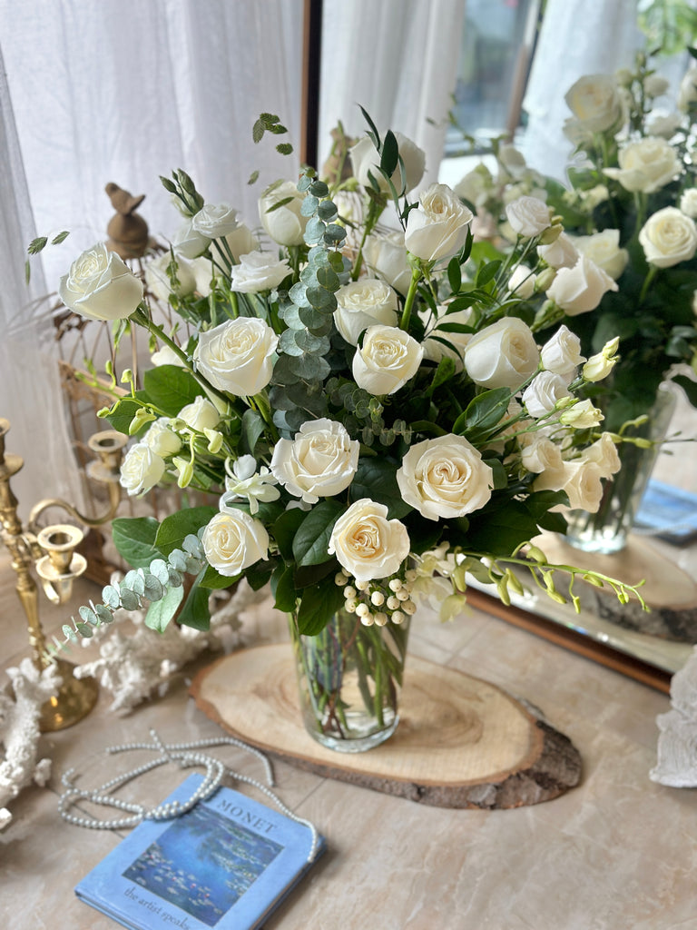Photo of white rose arrangement in a glass vase on a wood slab surrounded by decor