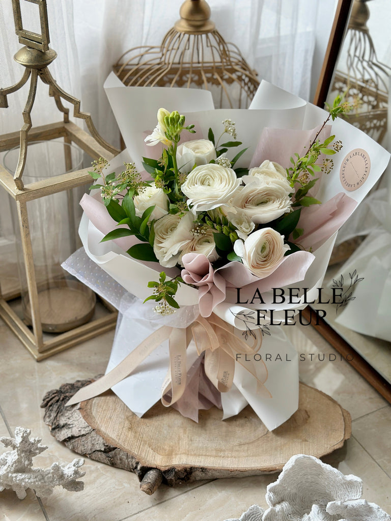 White ranunculus bouquet by La Belle Fleur wrapped with paper and ribbons and displayed amongst decor items