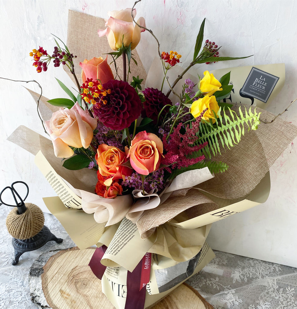 photo-of-La-Belle-fleur-s-sunrise-fall-flower-bouquet-with-colourful-mixed-flowers-wrapped-in-paper-sitting-on-a-wood-slab
