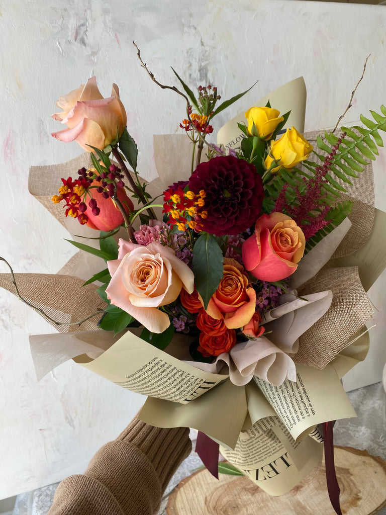 photo-of-a-hand-holding-La-Belle-fleur-s-sunrise-fall-flower-bouquet-with-colourful-mixed-flowers-wrapped-in-paper