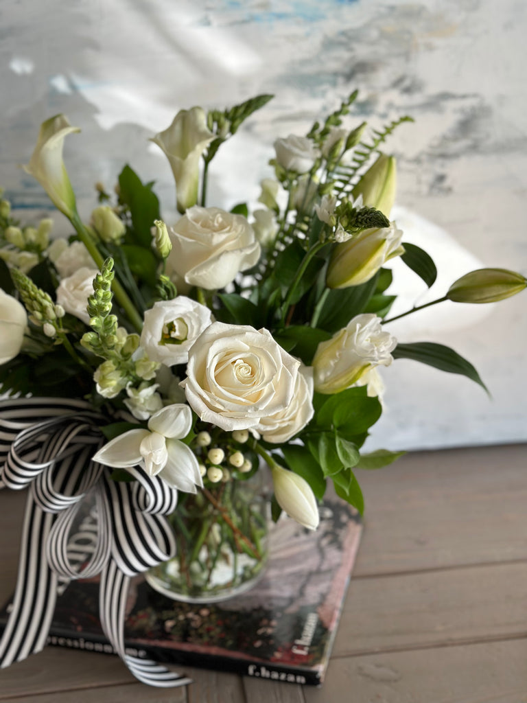 Close-up photo of the Peace Sympathy white flowers arrangement in a glass vase with a black and white ribbon bow tie