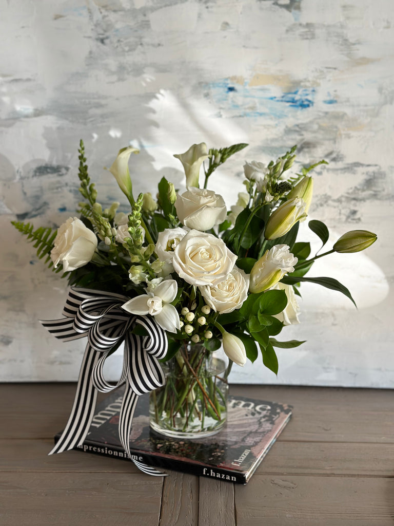 Photo of the Peace Sympathy Arrangement with a ribbon bow in a glass vase set on top of a book